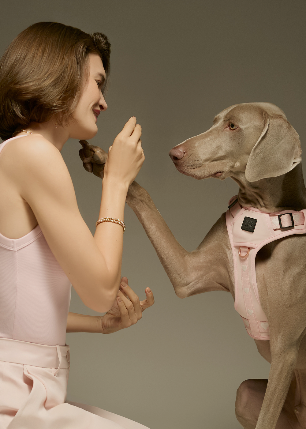 Vertical mobile banner showing a heartwarming moment between a woman and her dog wearing a designer pink heart-patterned harness.