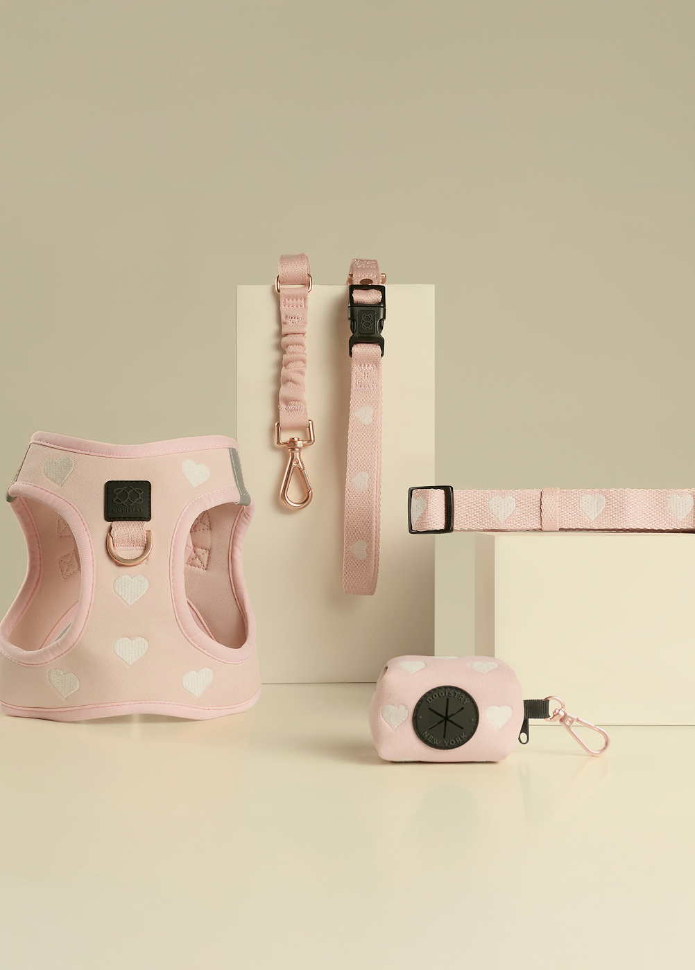Complete Dogistry pink heart-patterned collection featuring a padded step-in harness, matching collar, leash, and a stylish waste bag dispenser.