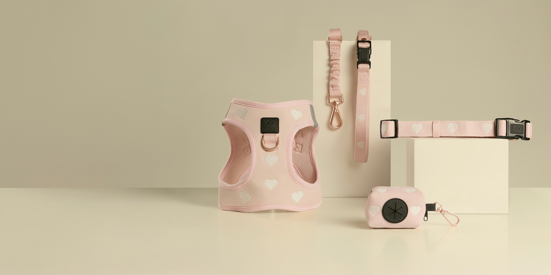 Complete Dogistry pink heart-patterned collection featuring a padded step-in harness, matching collar, leash, and a stylish waste bag dispenser.